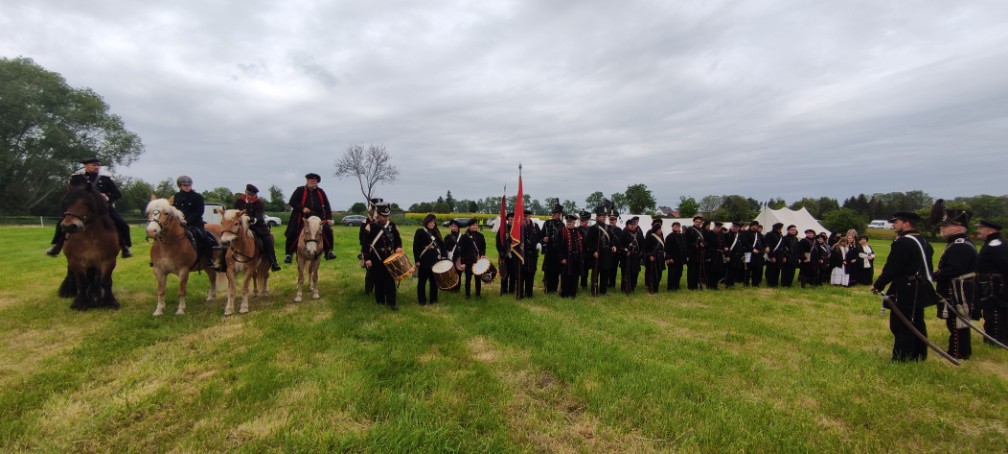 Angetretene Formation in schwarzen Uniformen mit Reitern, Trommlern und der schwarz-roten Fahne